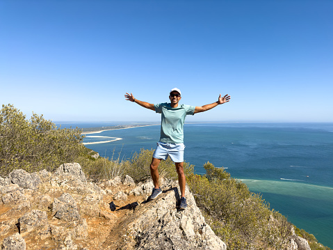 Man with open arms smiles for photo with a beautiful ocean landscape in the background