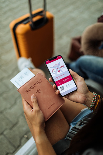 Close-up of phone, passport, and ticket with a suitcase in the background