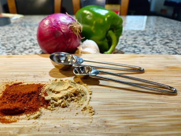 Spices, Vegetables And Measuring Spoons  Sitting On Cutting Board