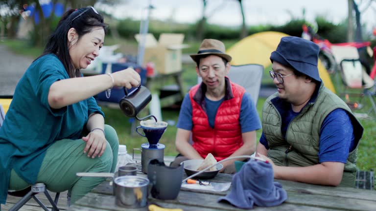 Friends get up early and drink a cup of hot coffee while camping in the mountains