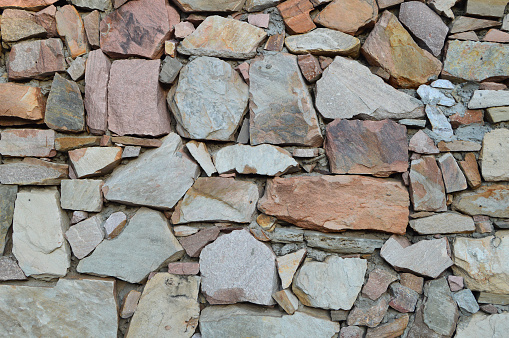 Bright horizontal picture of a heap of different sized cut abstract shaped rock Stones or rocks grey and brown colour gradient making a stone wall. The background is bright, has no people and no text.