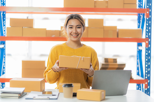 Beautiful Asian startup owner stays happily at home with packages on SME supply chain, purchasing, omnichannel purchasing or online selling ideas at home.