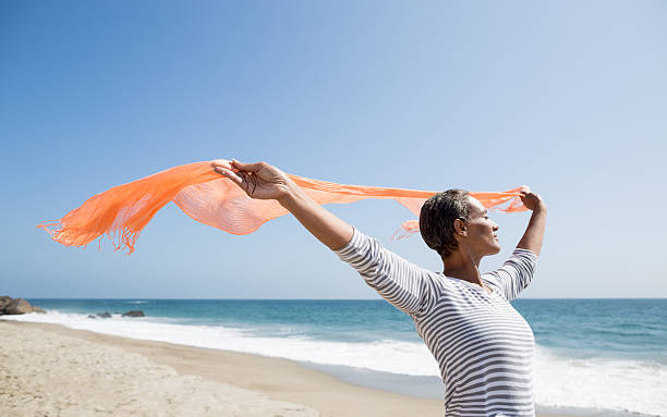 mujer mayor disfrutando de la playa - wind scarf women people fotografías e imágenes de stock