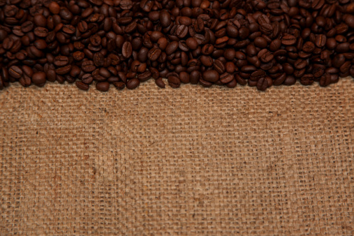 Coffee cup filled with coffee beans on rustic burlap background