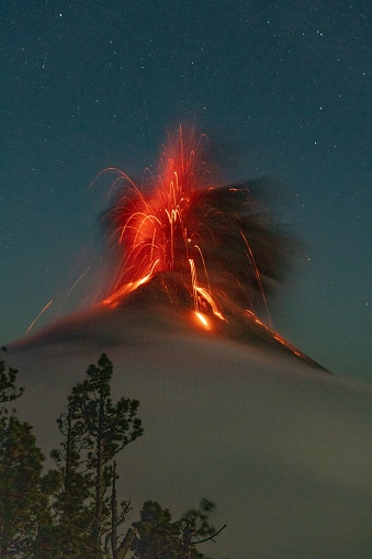 A blazing fire illuminates a misty mountain peak, under a starfilled sky.