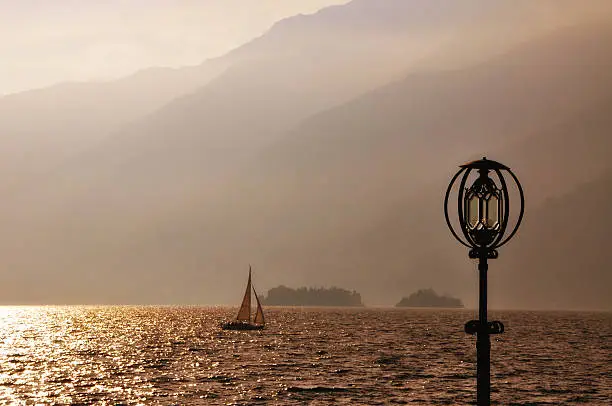 Alpine lake with a sailing boat and island and a lighthouse in ticino switzerland