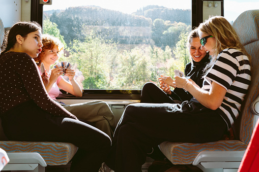 group young teenage girls traveling by train across Europe, sitting together, playing cards.