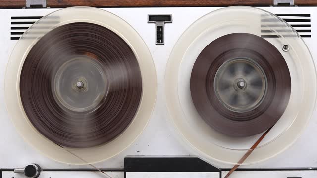 Old reel-to-reel tape recorder rewinds magnetic tape, vintage music player close-up