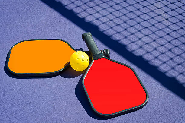Pickleball - Two Paddles and A Ball in Net Shadow Imae of 2 Pickleball paddles and a pickleball laying on pickleball court with net shadow. pickleball stock pictures, royalty-free photos & images