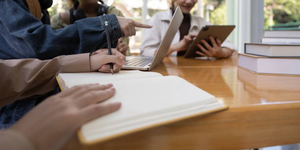 istock University students sitting together at table with book and laptop. Happy young people doing group study in college campus 1772091384