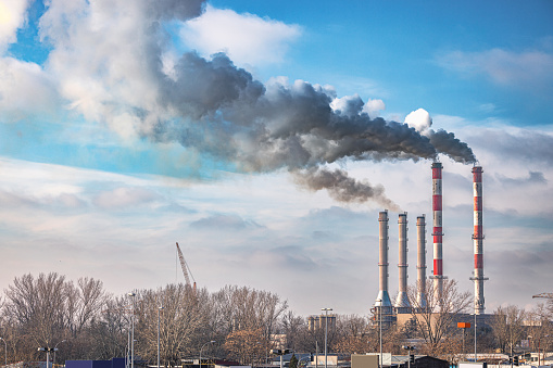 Industrial area, red and white tall chimneys in industrial plant polluting the area with black smoke, cloudy blue sky above