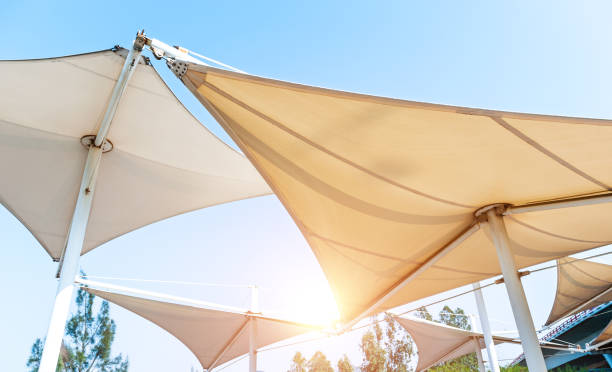 weiße markisen in segelform unter blauem himmel - shade sail awning textile stock-fotos und bilder