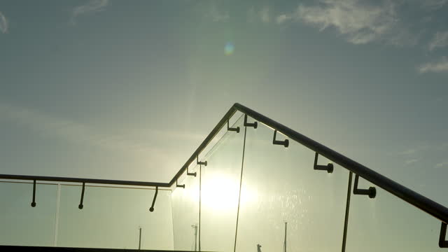 Sun shining through a sleek glass railing, silhouette of masts in the background