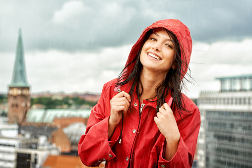 Pretty young woman smiling while wearing a red raincoat - portrait