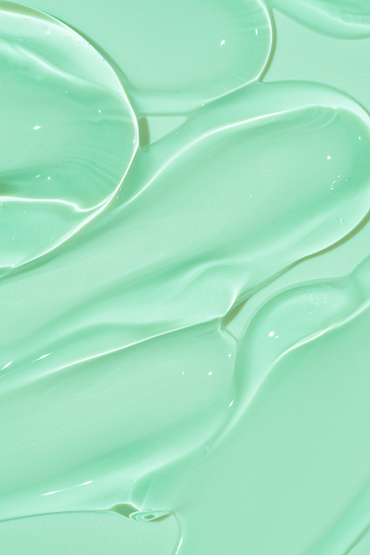 cosmetic smears cream texture on green background. Beauty serum drop. Transparent and creamy skin care product sample