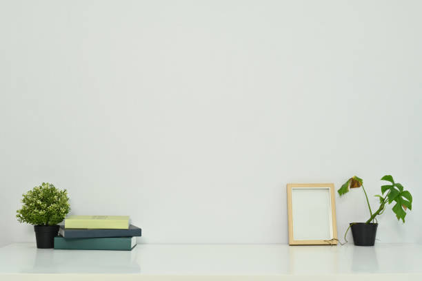 istock Minimal workplace with books, coffee cup, photo frame and potted plants on table against a clean white wall 1772181463