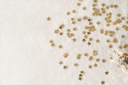 Aesthetic Christmas, New Year party celebration background. Gold star confetti pattern on neutral beige linen texture fabric backdrop.