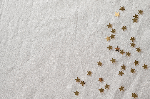 Minimalist aesthetic festive New Year or birthday celebration background with copy space. Golden glitter confetti stars scattered on neutral beige linen tablecloth. Holiday party backdrop, banner.