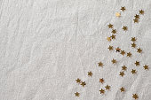 Minimalist aesthetic festive New Year or birthday celebration background with copy space. Golden glitter confetti stars scattered on neutral beige linen tablecloth. Holiday party backdrop, banner
