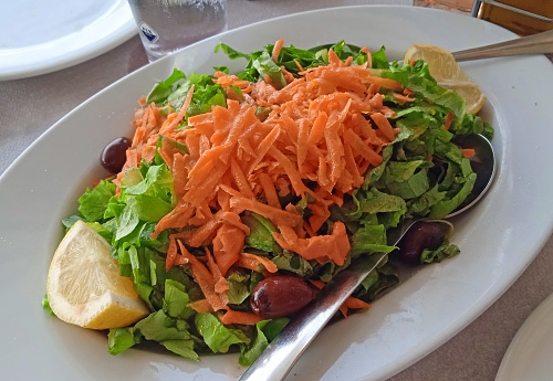 Green salad with grated carrot and lemon wedges on a platter
