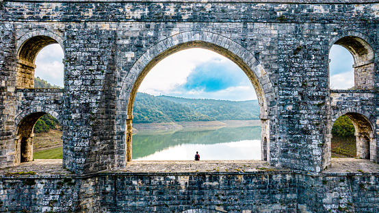 Aerial drone photo of two tourist sitting on the arch of the historical bridge, historical cavlova aqueduct, Maglova Aqueduct is one of the unique aqueducts in Istanbul. It is one of the most preferred aqueducts for weekend exploration trips in Istanbul.