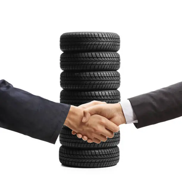Auto mechanic and a businessman shaking hands in front of a pile of vehicle tires isolated on white background