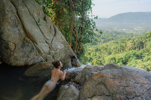 Woman in white swimsuit swimming in tropical waterfall on  Ko Samui