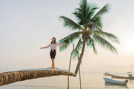 Young  woman  balancing while walking on coconut palm tree on the beach