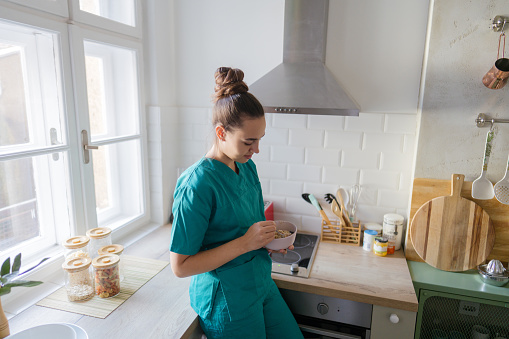 Photo of a female healthcare professional still in her medical scrubs, eating a home cooked meal in her kitchen