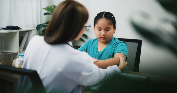 Footage shot, Selective focus, Young female doctor checking teenager's blisters arm, use tablet while explaining in examination room, Professional Healthcare Dermatology Check-Up with Teenage Patient