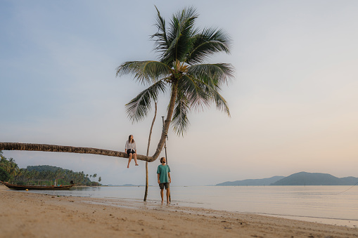 Man and woman on bent coconut palm tree on tropical beach