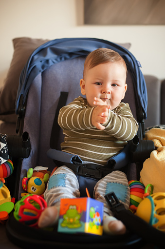 Portrait of cute baby boy in pram baby carriage, surrounded with colorful toys. Love and family emotion