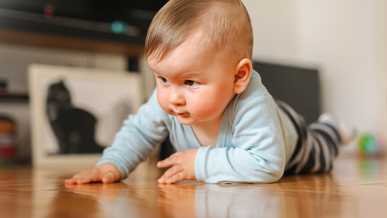 Cute baby boy crawls on the home floor, explore the world and learn to move. Front view. Love and family emotion