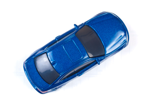 Miniature shiny blue toy car shot from above on white background