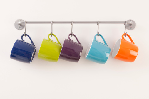 Assortment of bright color coffee mugs hanging on a metal rack.