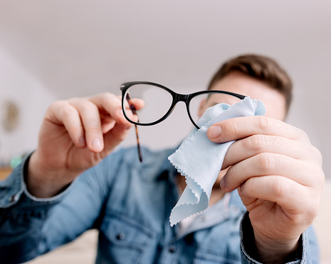 A man meticulously cleaning his eyeglasses with a soft cloth, ensuring clarity and maintenance.