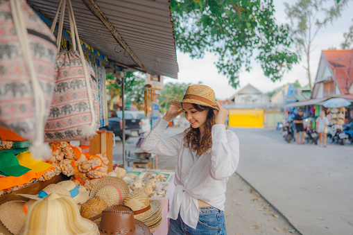 Woman buying straw w hat in souvenir shop in Thailand