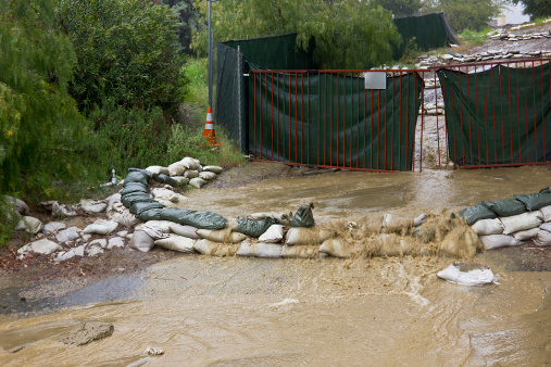 Sandbags overrun by heavy rain with a gate in the background.