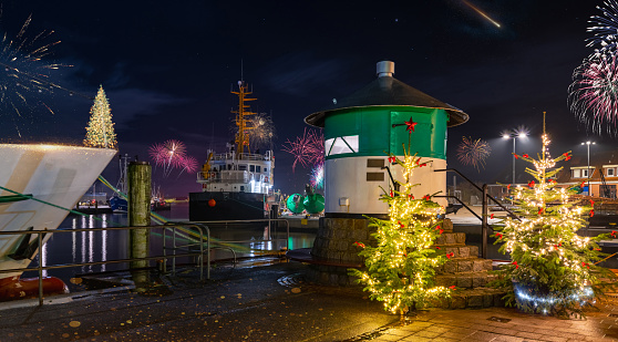 Green pier light, cristmas trees and fireworks in the fishing port of Büsum on the German North Sea coast. The romantic atmosphere of New Year's Eve in Büsum at night with fireworks.