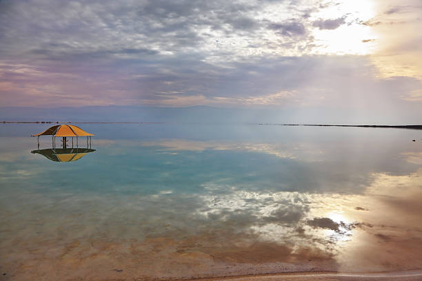 The picturesque red gazebo in the water near the shore. Excellent optical effects and reflections of clouds and sun in the water. Winter in the Dead Sea
