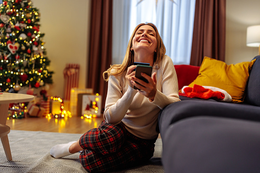 Young woman is sitting on the floor of her home, enjoying her online Christmas shopping while holding a credit card