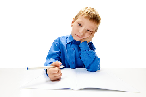 Boring little boy of elementary class doing his homework. Child study and learn for preschool. Online education. Concept of childhood, International Knowledge Day, study. Copy space for ad, text.