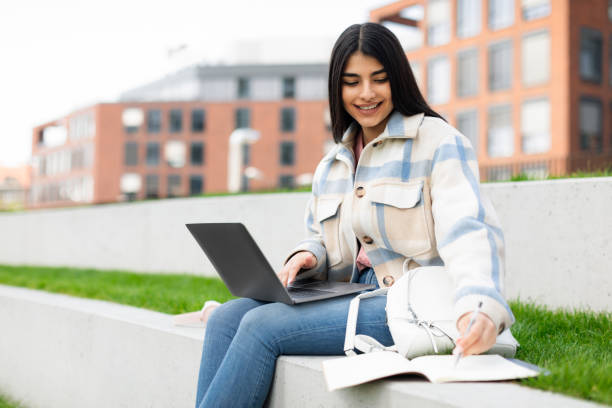 istock Cheerful student lady doing homework or preparing for test outdoors, learning with laptop and copybook, copy space 1772367031
