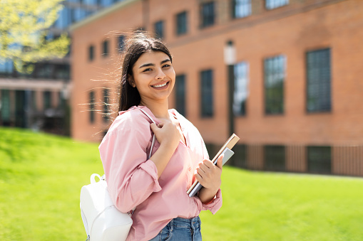 Portrait of glad lady student in casual with books posing outdoors and smiling at camera, ready for lesson in university campus, free space. Study, knowledge at college