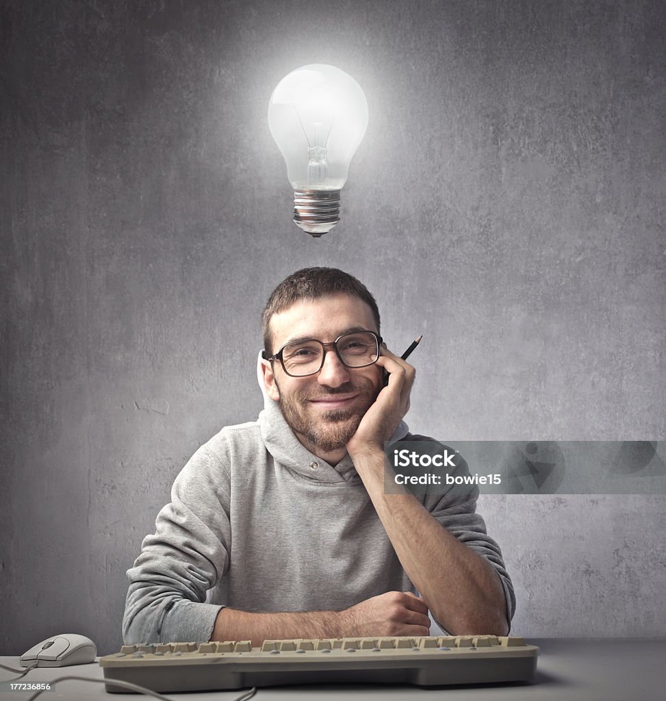 Creative programmer Smiling young man in front of a computer keyboard with light bulb over his head Computer Stock Photo