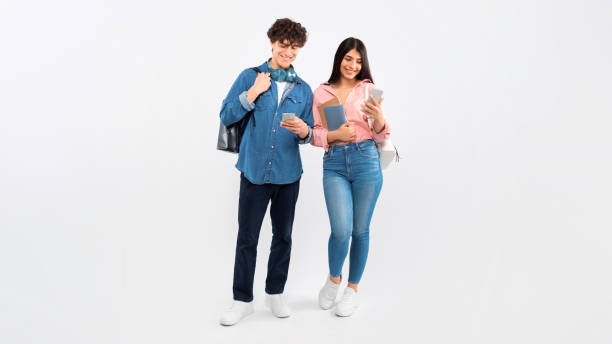 istock Cheerful Young Students Couple Using Phones On White Studio Background 1772369426