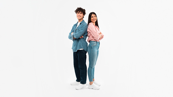 Happy Young Couple Posing Standing Back To Back Smiling To Camera Over White Background. Full Length Shot Of Boyfriend And Girlfriend Expressing Positive Emotions. Youth And Friendship. Panorama