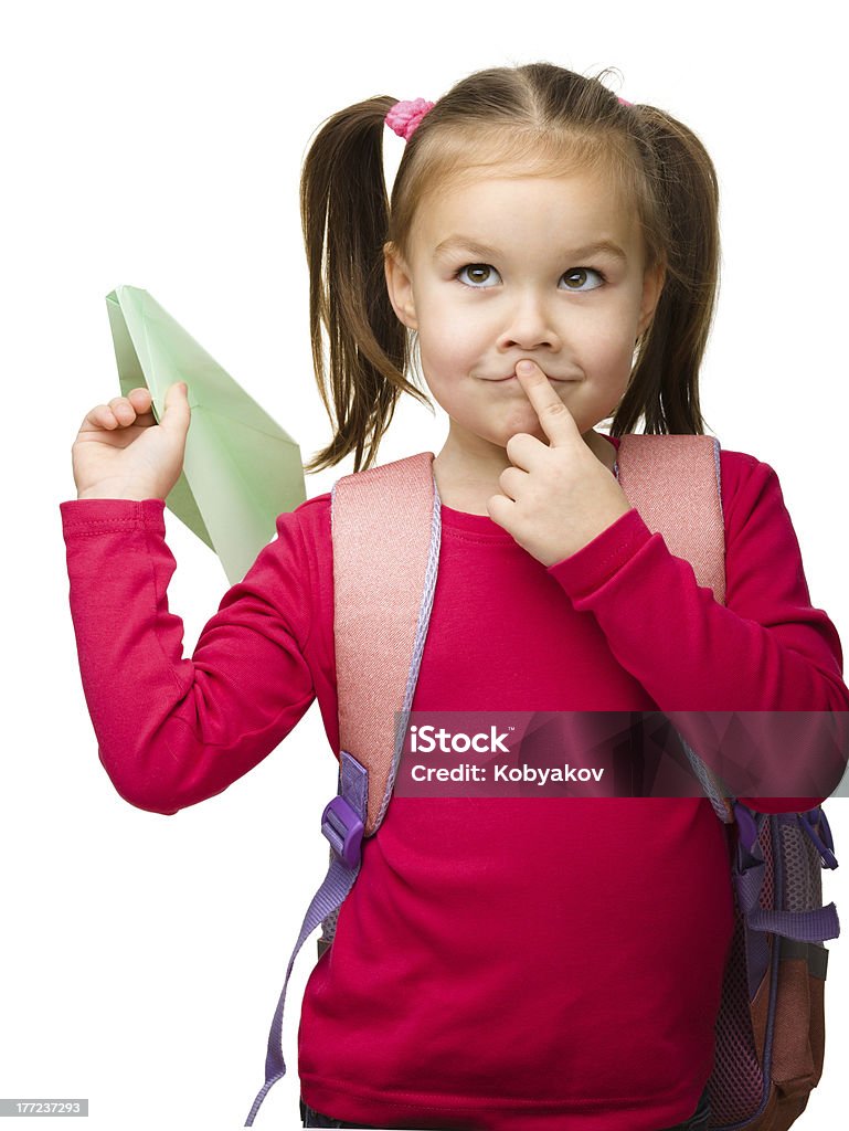 Portrait of a cute schoolgirl with backpack "Portrait of little schoolgirl with backpack thinking about something and going to throw a paper airplane, isolated over white" 2-3 Years Stock Photo