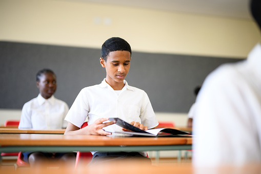 Young teenage schoolboy in class sitting at desk opening text book