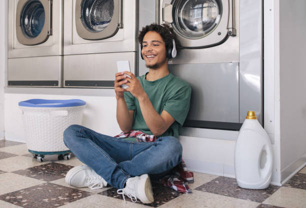 chico usando smartphone lavando ropa en la máquina en el servicio de lavandería - all laundry detergent audio fotografías e imágenes de stock